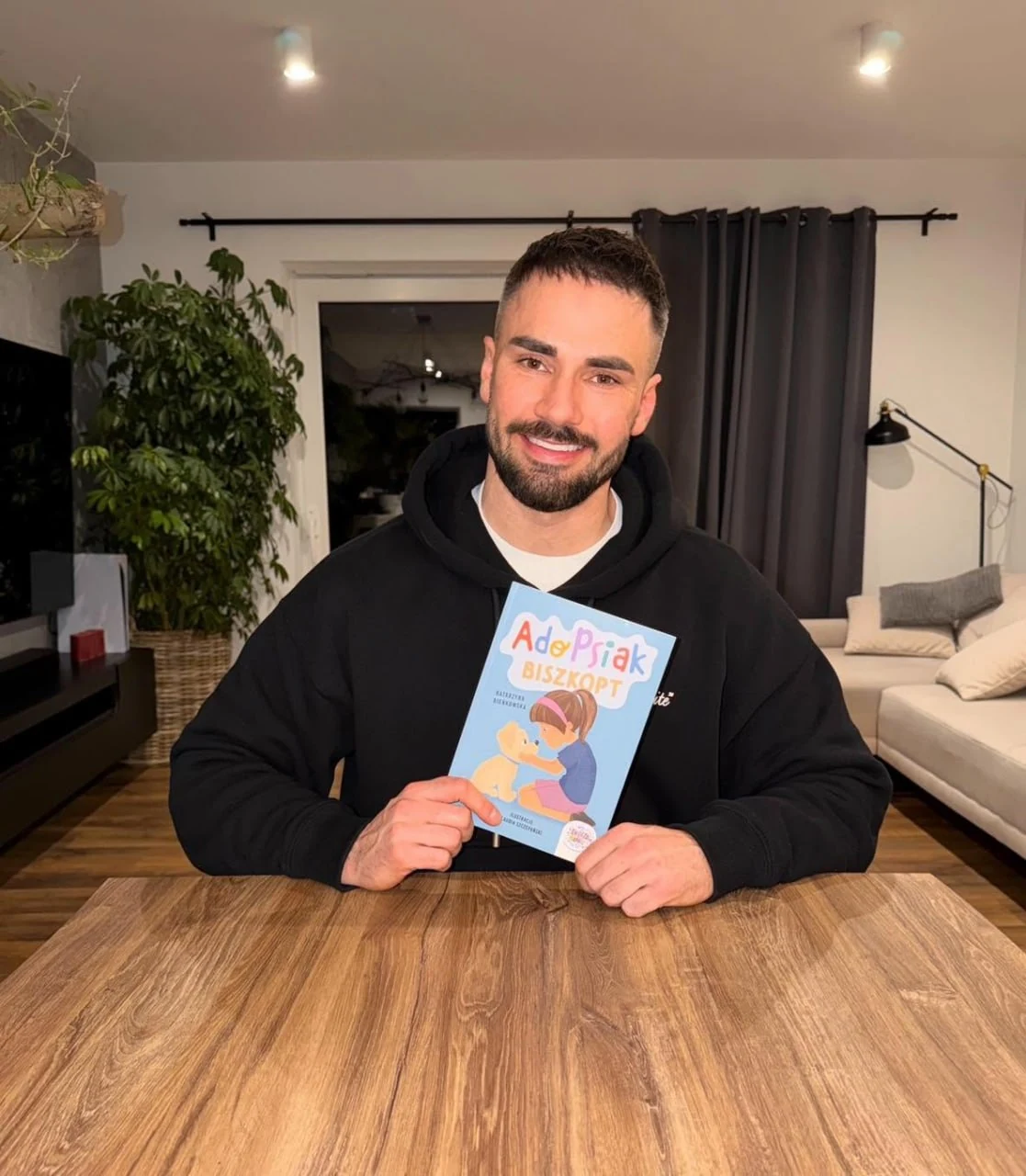 Łukasz Litewka sosteniendo el libro «AdoPsiak Biszkopt»